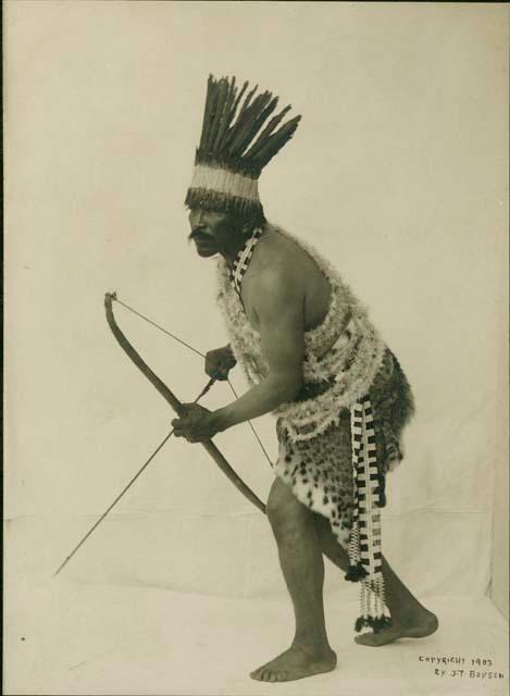 Staged studio portrait of Maidu Indian hunting with bow and arrows