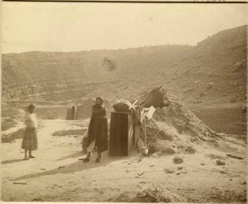 Navajo woman and girl standing in front of a hogan