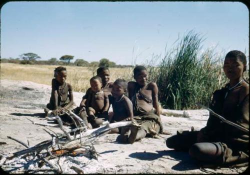 !Ungka sitting with a group of women and children on a ledge near a waterhole