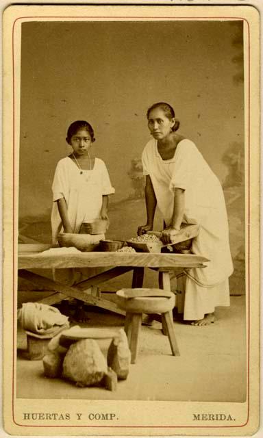 Studio-staged scene of a Maya woman and child making tortillas