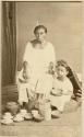 Studio portrait of Maya woman and child, seated on floor with dinnerware