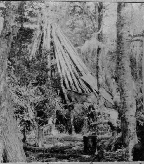 People by hut enclosure made of branches