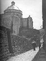 People walking near stone wall, building with dome