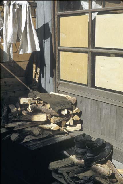 Wood stacked against side of building, boots on top of stack