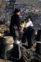 Woman and children on hill with tea kettle and containers