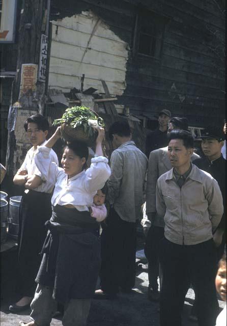 People in street, woman with basket of greens on her head