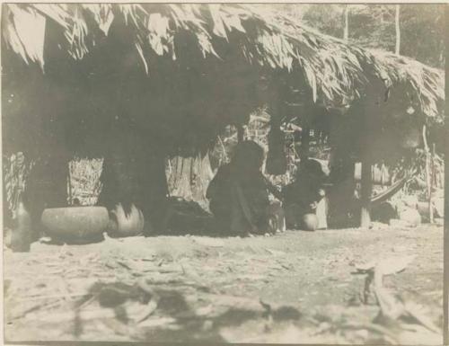 Silhouetted figures and pottery beneath hut\