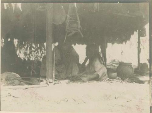 Adult and child seated beneath hut