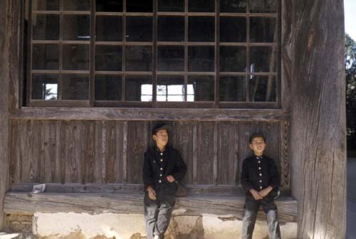 Boys sitting beneath a window outside of a building