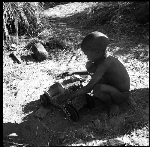 Child playing with a toy car made from an expedition file box and film reels