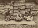 "Making Kava" - a woman and two men seated on mat, woman holds kava root and men hold bowls