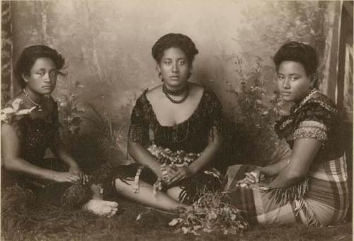 Three Samoan women seated in front of backdrop, wearing formal tops and jewelry