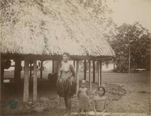 Woman and girls beside grass house