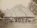 Woman and two girls stand in front of grass house, or fale tele