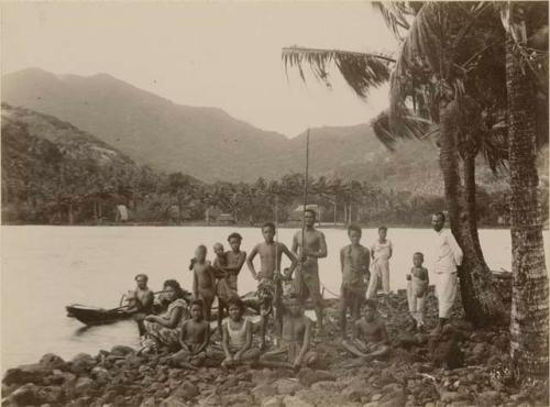 Group of people gathered on rocky shore, two in canoes close by