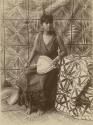Samoan woman posed holding a fan, tapa cloths behind and beside her