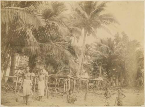 Young Samoans standing on beach beside drying frames