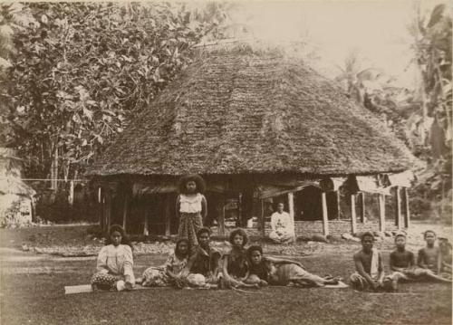 Young Samoan women (singers), posed with house in background, boys to the side