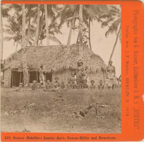 Group posed for portrait, grass house behind them