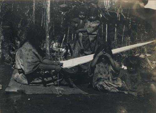 Woman on loom, children seated around her