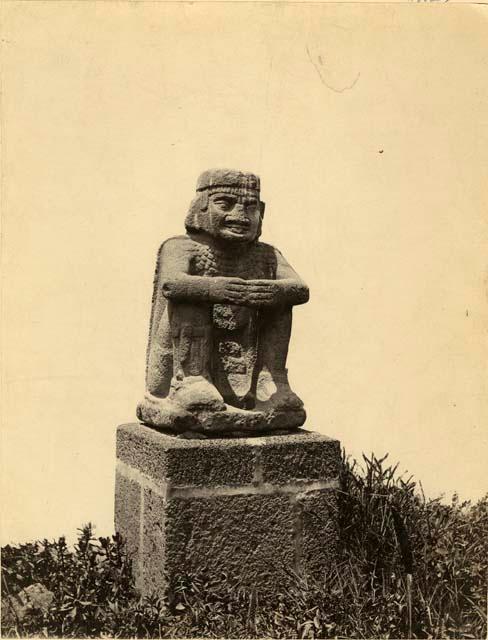 "Statua del Indio" - Stone carving of seated man, tongue between teeth, elaborate necklace