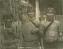 Three men with long earrings and beaded necklaces, holding staffs