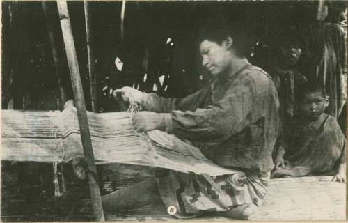 Person weaving with a loom, and children in background