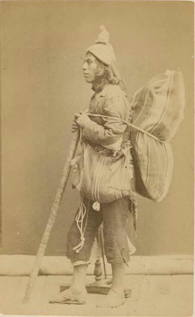 Man with walking stick carrying a large woven bag