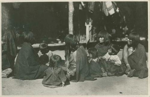 Women and children sitting in front of a structure