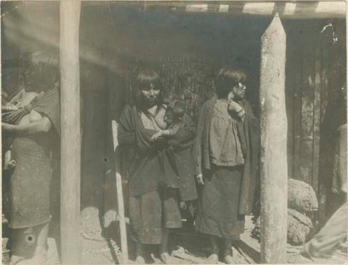 Three women standing in a structure, two with babies