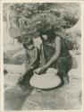 Woman making clay pot with child watching