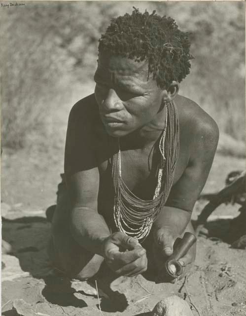 ≠Toma crouching and holding a soapstone pipe (print is a cropped image)