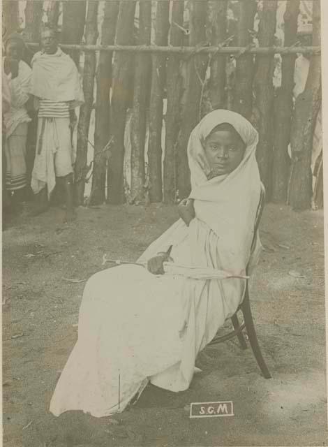 Woman sitting in front of fence or structure, with two men in background