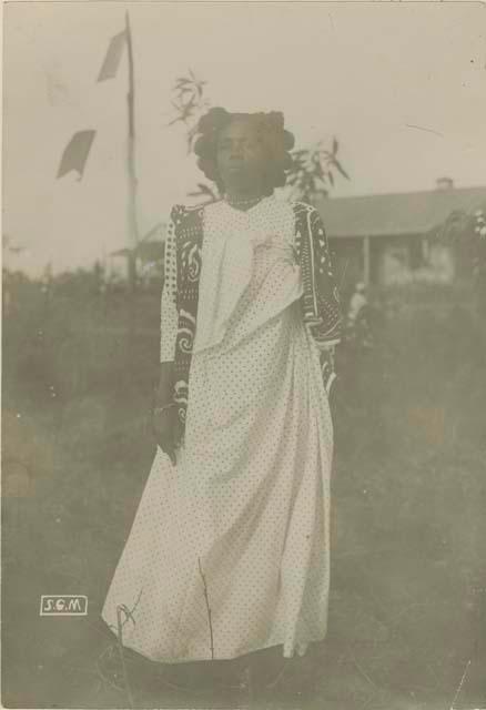 Sakalave woman standing, with building and flag in background