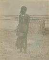 Woman standing, with hut in background