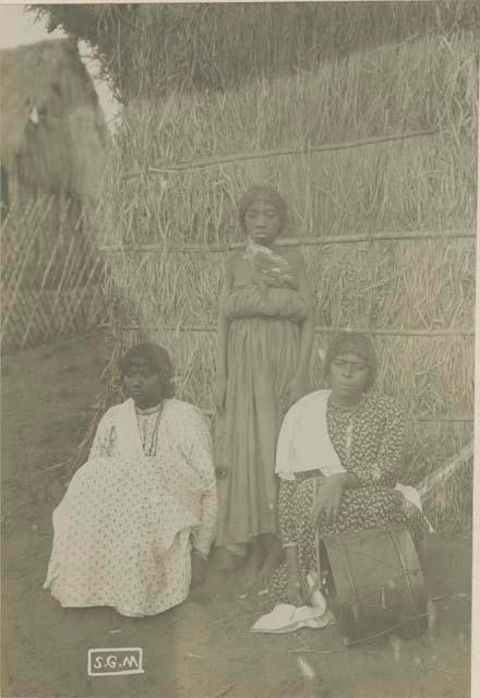 Three women in front of a hut