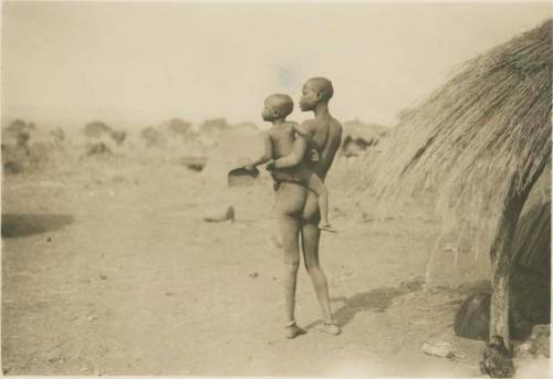 Woman holding child next to hut