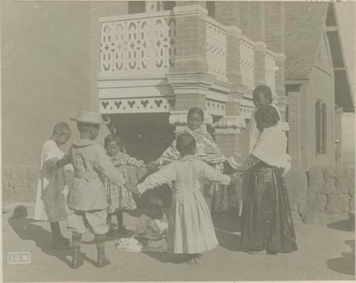 Children holding hands in a ring in front of a building