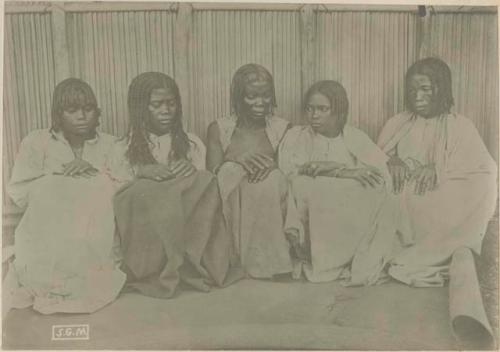 Five women sitting in front of a fence or wall