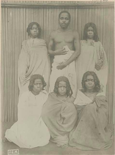 Man and five women standing in front of a fence or wall