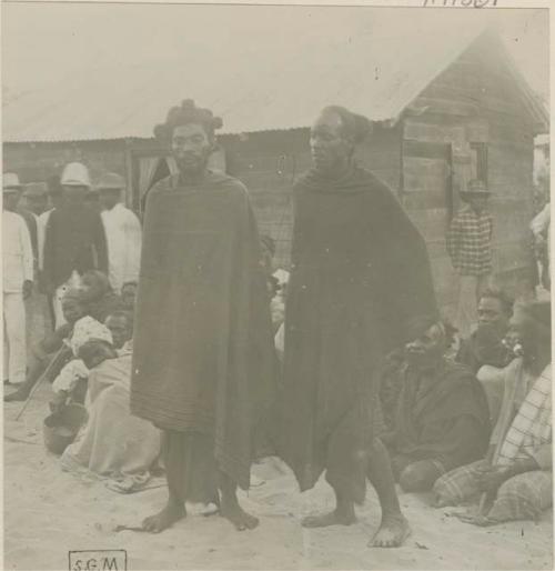 Two men standing, with group in background