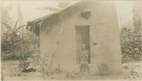 Woman sitting in doorway of hut protected by charms