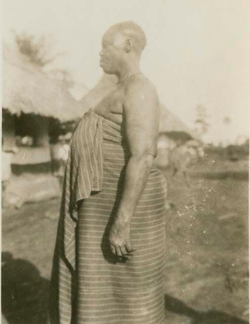 Woman standing, with hut in background