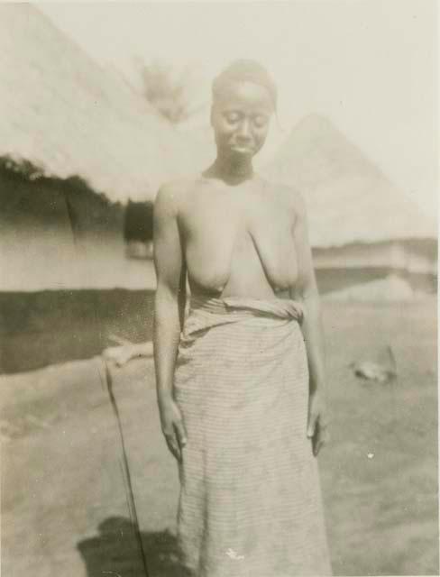 Woman standing, with huts in background