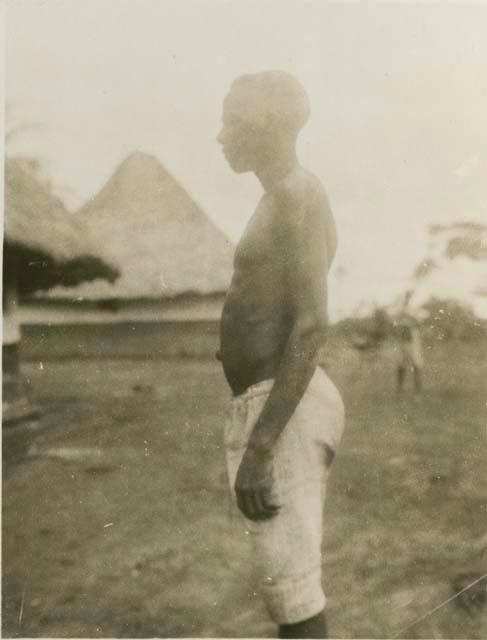 Man standing, with huts in background