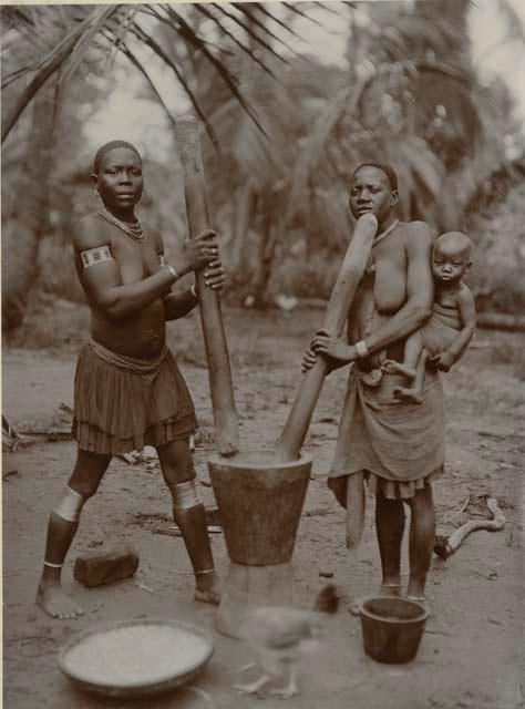 Two women grinding maize, one with a baby in a sling