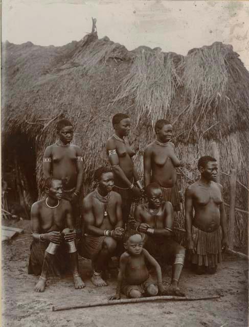 Group of women and a child posed in front of a hut