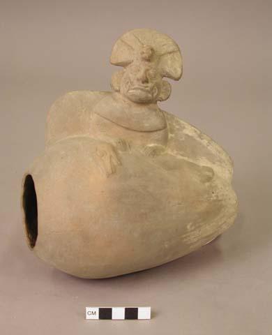 Shell shaped pot with fanged anthropomorphic figure holding snake-like animal.