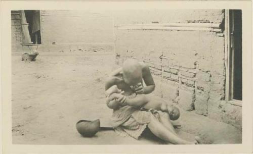 Woman giving child an enema with a gourd