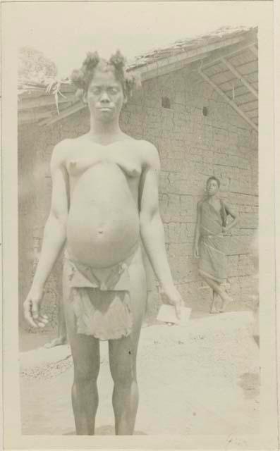 Woman standing in front of hut, with man in background